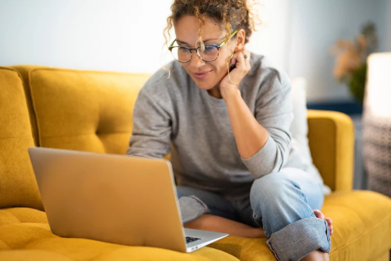 Woman sitting on a couch using a laptop to research inpatient rehab options in Virginia.
