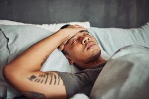 Man lying in bed with his hand on his forehead, appearing unwell with symptoms that can occur during early alcohol withdrawal.