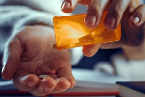 Person pouring tablets from an orange prescription bottle into their open hand.