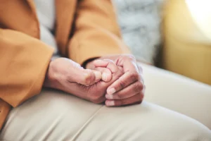 Close-up of two people holding hands while seated together on a couch.