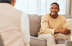 Person seated on a couch in conversation with someone sitting across from them.