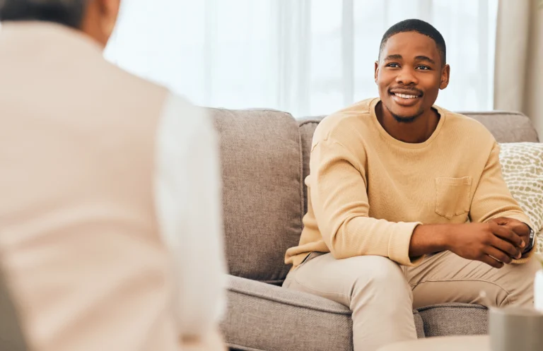 Person seated on a couch in conversation with someone sitting across from them.